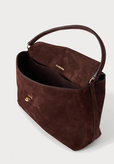Sac à main en daim brun foncé avec une anse unique, ouverture sur le dessus dévoilant une poche intérieure, et logo doré « Sandro » embossé à l'intérieur et sur le fermoir avant.