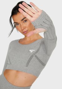 Gray long-sleeve crop top with thumbholes, featuring a textured knit and geometric accents. Logo displayed on the chest area.