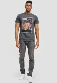 Grå bomulls t-shirt med en färgglad grafisk tryck med rymdtema. Kombinerad med grå slim fit-jeans och vita sneakers.