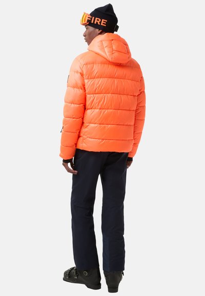 Pomarańczowa pikowana kurtka z kapturem, z wyprofilowanymi sekcjami. Połączona z granatowymi spodniami i czarnymi butami. Czarna czapka z napisem "FIRE" i goglami.