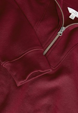 Burgundia dressipluus hõbedase tõmbluku ja soonikute cuffs'iga, millel on sile tekstuur. Etiketil on suurus M ja brändi nimi "THE SET."