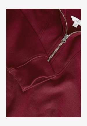 Burgunderfarbener Sweatshirt mit silbernem Reißverschluss, ausgestattet mit gerippten Bündchen und einer glatten Textur. Das Etikett weist die Größe M und den Markennamen "THE SET" aus.