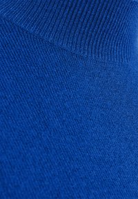 Blau gestrickter Stoff mit einer strukturierten Oberfläche und geripptem Kragen. Nahaufnahme hebt die Tiefe und den Reichtum der Farbe hervor.