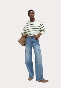 Randig grön och vit långärmad topp med krage, kombinerad med vida blå cargo-jeans med sidofickor.