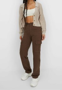 Bruna cargobyxor med sidfickor och rak bendesign, i kombination med en ljusbeige stickad kofta och vita sneakers.