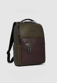 Bruine en olijfgroene leren rugzak met een bovenhandvat, gevoerde schouderbanden, een voorvak met ritssluiting en een rechthoekige vorm. Opvallende hardware-accenten.