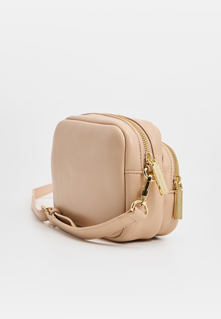 Kwadratowa, brązowa torba crossbody wykonana z miękkiej skóry, z dwoma zamykanymi na zamek przegródkami, złotymi akcentami oraz płaskim, regulowanym paskiem. Gładka tekstura.