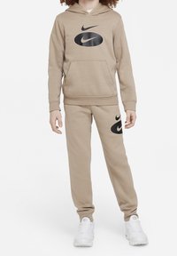 Béžová mikina Nike s velkým černým logem na přední straně, doplněná o odpovídající béžové tepláky s logem na levém stehně.