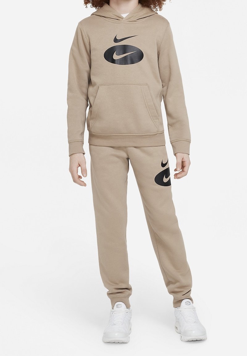 Béžová mikina Nike s velkým černým logem na přední straně, doplněná o odpovídající béžové tepláky s logem na levém stehně.