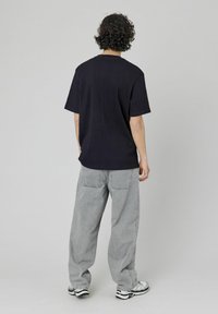 Chemise courte à manches courtes oversize bleu marine avec une finition texturée, associée à un jean gris clair ample et des baskets sportives noir et blanc.