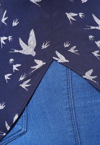 Námořnická látka s bílým vzorem ptáků na vrchu přechází do modrého denimu na dolní části. Má špičatý lem a prošité švy.