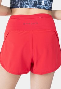 Czerwone spodenki sportowe o gładkiej fakturze, z wysokim stanem, dwoma bocznymi kieszeniami i logo "SPYDER" na plecach.