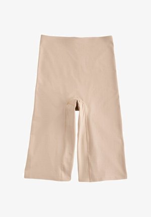 Közeli kép egy személyről, aki magas derekú, bézs színű, varrás nélküli biciklis rövidnadrágot visel, amely a combközépig ér, és középen hátul látható varrással rendelkezik.