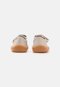 Vista posteriore di scarpe in tela beige con accenti grigi e chiusura in velcro. Presentano una suola in gomma flessibile e dettagli cuciti lungo i bordi.