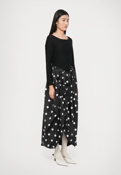 Must pikkade varrukatega särk, millele on kombineeritud täpiline seelik, millel on suur kangasroosi detail, lõpetatud valgete kontsakingade ja kreemikasvalgete sukkpüksidega.