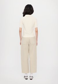 Short-sleeve cream polo shirt paired with loose beige pants, featuring two back pockets and a relaxed fit, complemented by white socks and sandals.