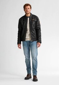 Svart skinnjacka med dragkedja framtill, beige stickad tröja, ljusblå jeans och bruna stövlar. Detaljer med axelpatch och dragkedjeficka framtill.