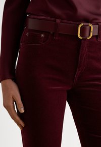 Bordowe jeansy ze sztruksu z pionowym prążkowaniem, posiadające dwie przednie kieszenie oraz dopasowany pasek ze złotą klamrą. Gładka faktura.