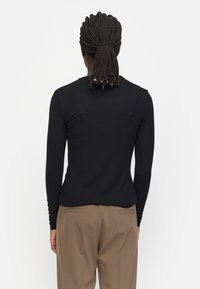 Sort langærmet top med tætsiddende design og ribbet tekstur, parret med lysebrune skræddersyede bukser med baglommer.