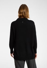 Mustaripaitainen neulepusero, jossa on ribbireunus kauluksessa ja helmoissa, sekä hienovarainen logokuvio selkäpuolella. Yli kokoa oleva malli, jossa pitkät hihat.