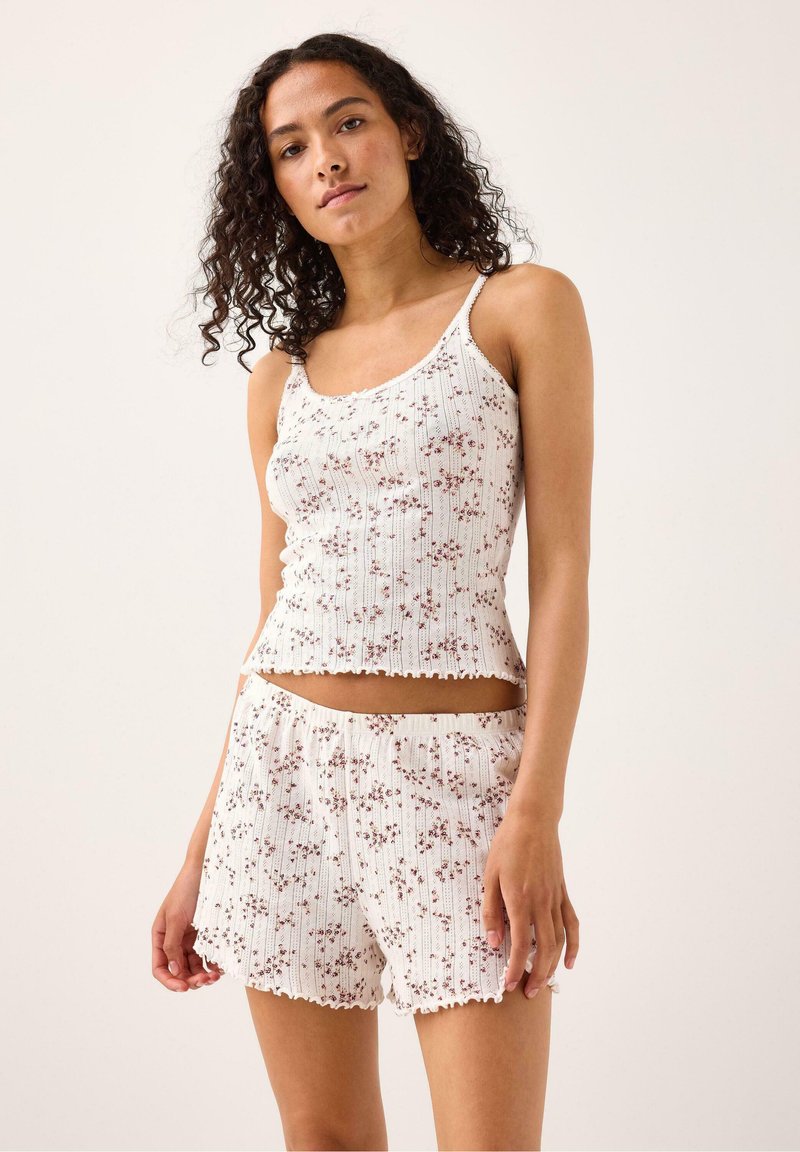 Vitt ribbat linne och shorts-set med små blommönster, vågiga kanter och justerbara spaghetti-band.