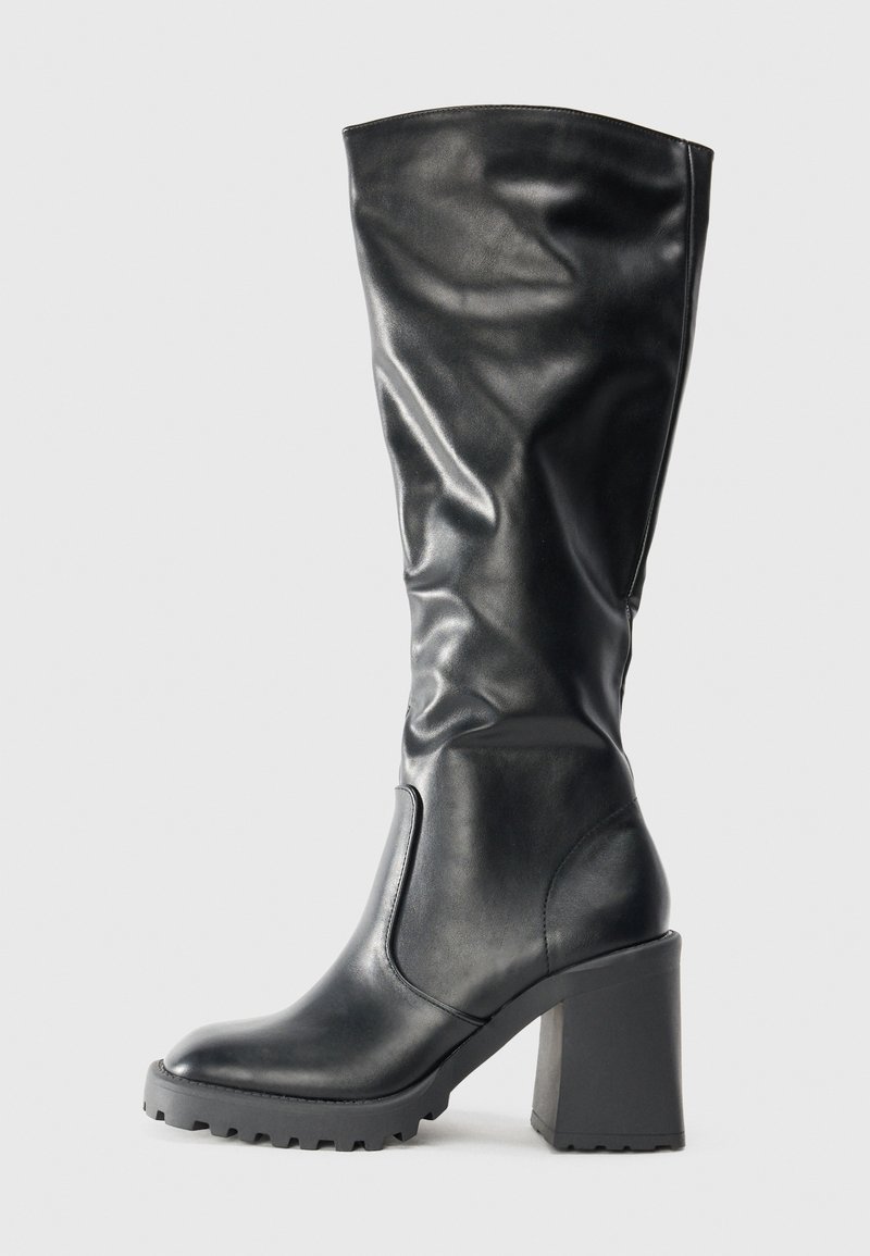 Bota de couro preta até ao joelho com bico arredondado, salto bloco robusto e sola texturizada, com um design macio e solto.