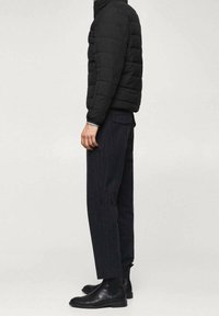 Veste matelassée noire avec un design capitonné, associée à un pantalon rayé foncé et des bottines noires. Silhouette simple et moderne.