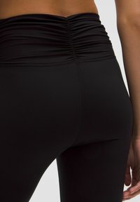 Fekete leggings ráncolt derékpánttal, sima elasztikus anyagból készült. Sima szélek és testhezálló kialakítás jellemzi.