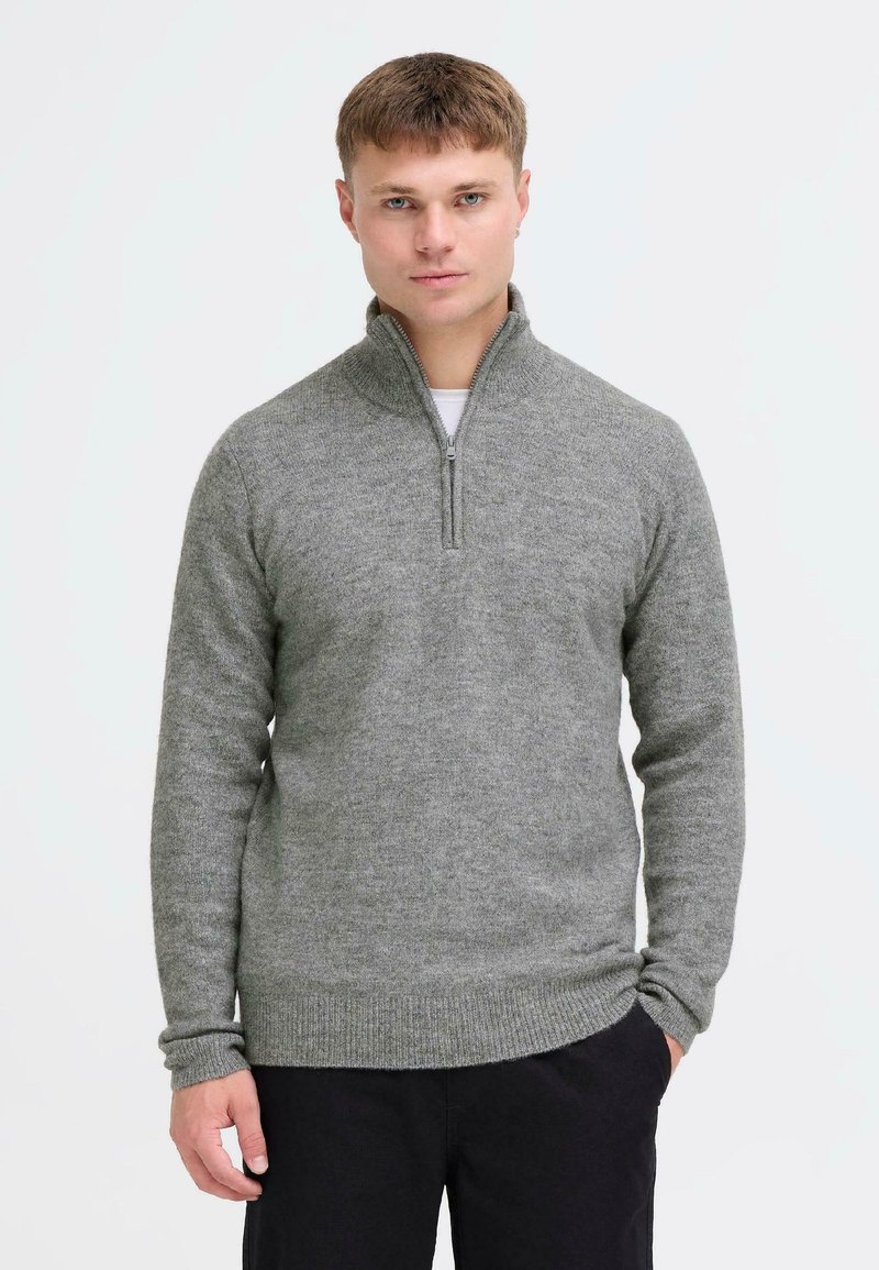 Harmaa neulottu pulloversi, jossa on neljännesvetoketjukaulus, pitkät hihat sekä ribbireunat hihoissa ja helmassa. Sileä pinta ja keskikoinen paino.