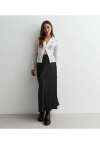 Witte kant lange mouwen top met een geknoopte voorkant, gecombineerd met een zwarte satijnen maxi rok. Zwarte chunky enkellaarsjes maken de outfit af.