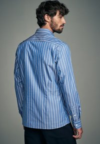 Blau-weiß gestreiftes Hemd mit langen Ärmeln und Knopfleiste am Kragen. Verfügt über vertikale weiße Streifen und einen geschwungenen Saum. Weiche Stoffstruktur.