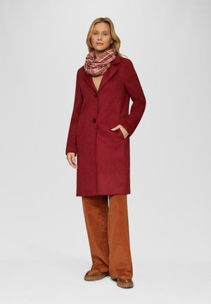 Rode wollen jas met een op maat gemaakt ontwerp, knoopsluiting met één knoop, zijzakken en een kraag, gecombineerd met een geruite sjaal en corduroy broek.