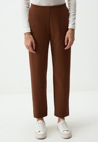 Pantaloni marroni su misura con un design elegante, caratterizzati da una trama liscia e una linea dritta. Abbinati a sneakers bianche.