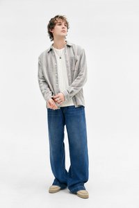 Grå og rosa stripete skjorte med knapper over en hvit ribbestrikket genser, parret med løse blå jeans og beige fottøy.