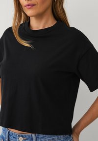 Černé zkrácené tričko s krátkými rukávy, kulatým výstřihem, vyrobené z hladké bavlněné látky, s volným střihem a minimalistickým designem.