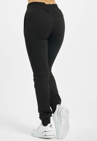 Sorte træningsbukser med en tapered design, elastisk talje og sidelommer, parret med hvide sneakers med sorte accenter.