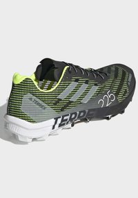 Czarne i neonowozielone buty biegowe z oddychającą siateczkową cholewką, teksturowanym wzorem, szarymi akcentami oraz solidną podeszwą zaprojektowaną dla lepszej przyczepności.