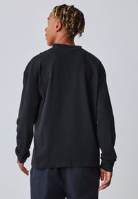 Sort langærmet T-shirt lavet af bomuld, med rund hals og løs pasform, med synlige syninger og en glat tekstur.