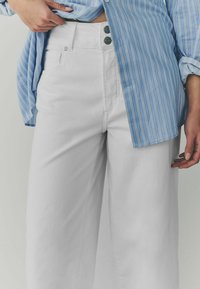 Witte hoge taille wijde jeans met een gladde textuur, voorzien van twee groene knopen aan de voorkant en een klassieke vijf-pocketontwerp.