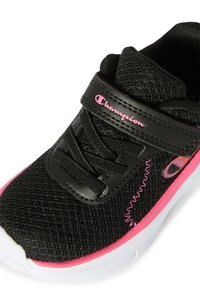 Scarpa sportiva nera con tomaia in mesh testurizzato e dettagli rosa. Presenta una fascia e lacci, con una suola bianca e un logo distintivo.