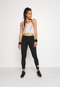 Gray camouflage crop top and black leggings with white logo. Outfit made of stretch fabric, designed for fitness, with a fitted silhouette.