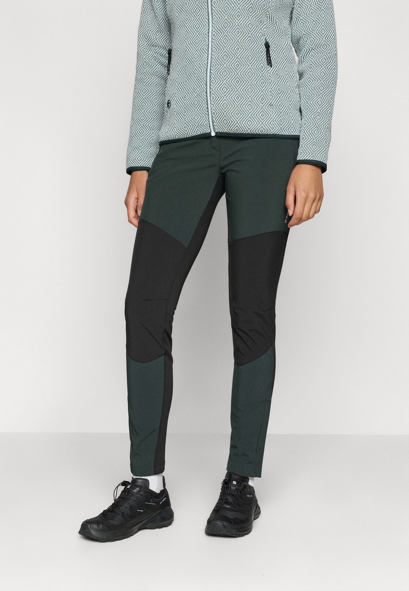 Dopasowane spodnie w ciemnozielonym i czarnym kolorze, z kontrastującymi panelami i gładką teksturą. W zestawieniu z czarnymi butami trekkingowymi.