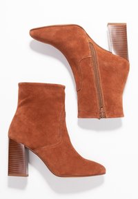Bottines en daim marron avec un bout pointu, fermeture éclair sur le côté et un talon bloc texturé. Fini lisse sans motifs visibles.