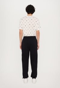 White t-shirt with black heart pattern, relaxed fit. Black sweatpants with elastic waistband, straight leg, side pockets, worn with white sneakers.