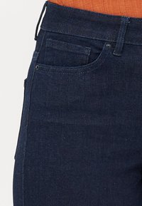 Temno modri denim kavbojki s klasičnim pet-pocket dizajnom, subtilnimi šivi in gladko teksturo.