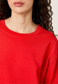 Raudonas medvilnės džemperis su apvalia iškirpte, vielos apykakle ir laisvu pritaikymu. Lygi tekstūra su minimaliai siuvimo detalėmis.