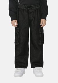 Czarne dżinsowe spodnie cargo z elastycznym pasem, dwiema dużymi kieszeniami bocznymi i luźnym krojem. Połączone z białymi butami sportowymi.