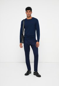 Suéter azul-marinho com decote redondo, combinado com calças azul-marinho a condizer. Inclui uma mala de ombro preta e sapatos pretos.