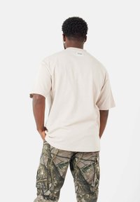 Lys beige bomuld t-shirt med en afslappet pasform, korte ærmer og et lille mærke på bagsiden. Sammen med camouflage cargo bukser med et struktureret mønster.