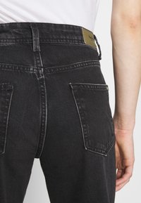 Černé džíny z denimu s mírně ošoupanou texturou, s mírně zvýšeným pasem, zadními kapsami a značkovou etiketou na pásku.